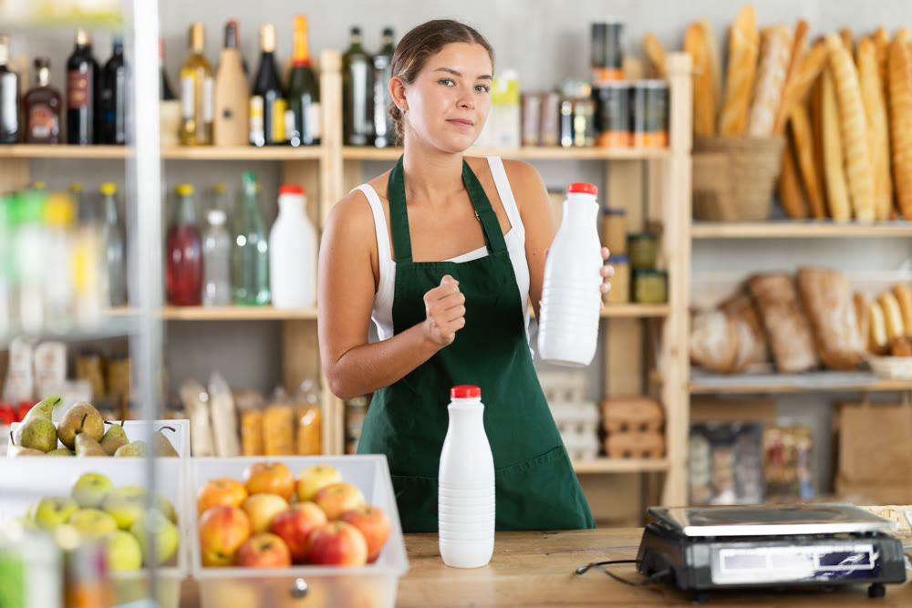 Young woman seller offering milk in grocery store
