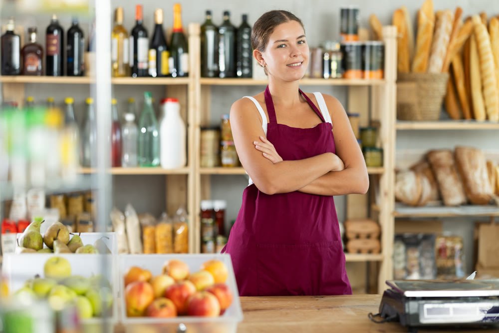Portrait of smiling female salesperson in apron behind supermarket counter