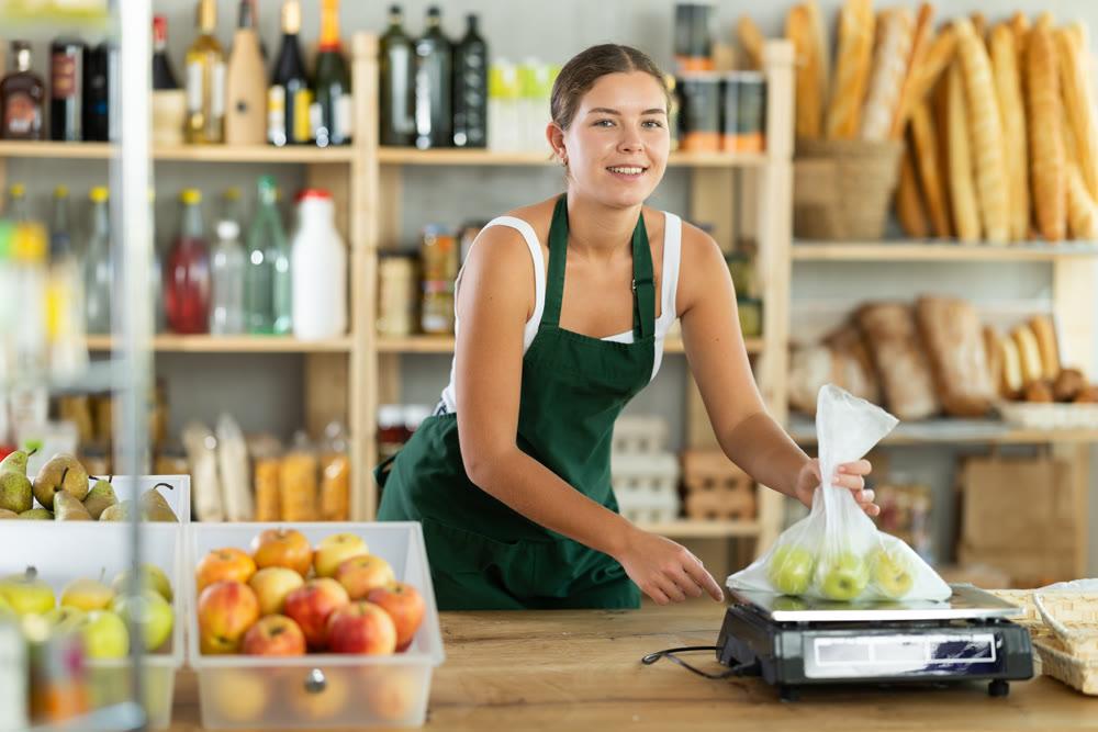 Young woman seller weighs apples in bag