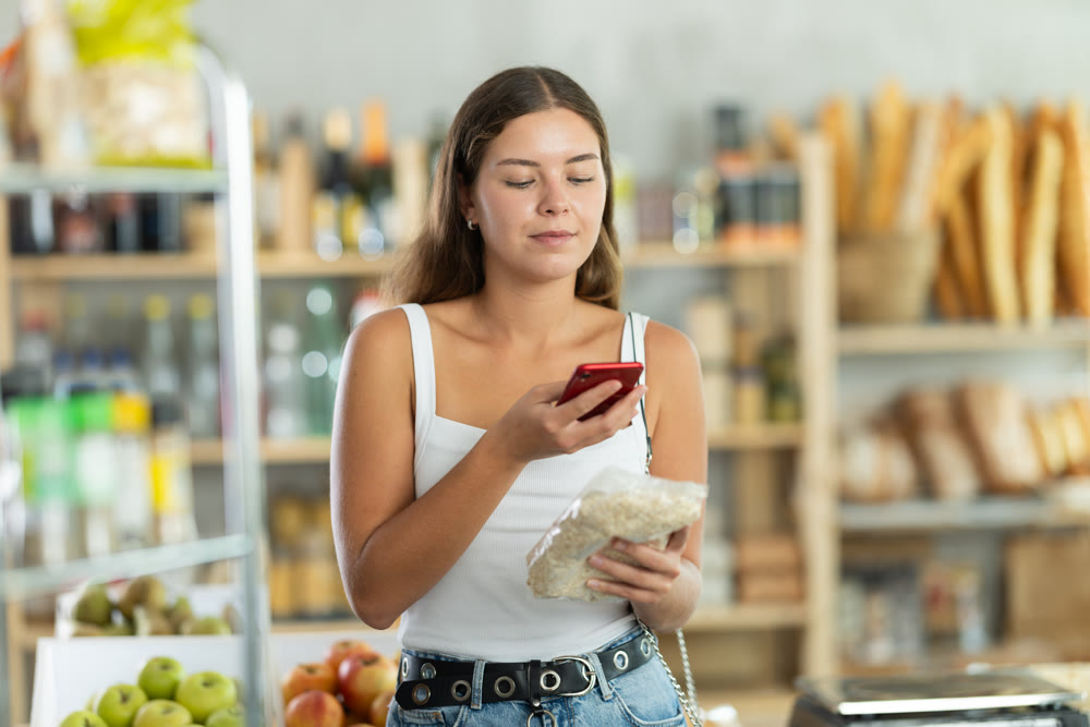 Female customer scans QR code on label oat flakes using smartphone. Checking products in supermarket