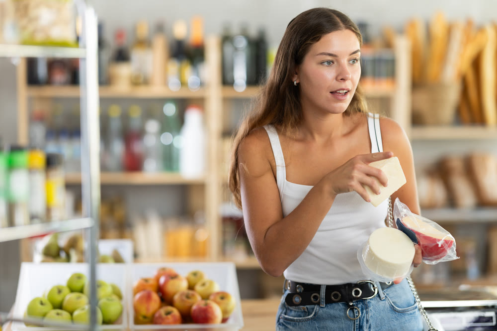 Young woman choosing cheese in grocery store