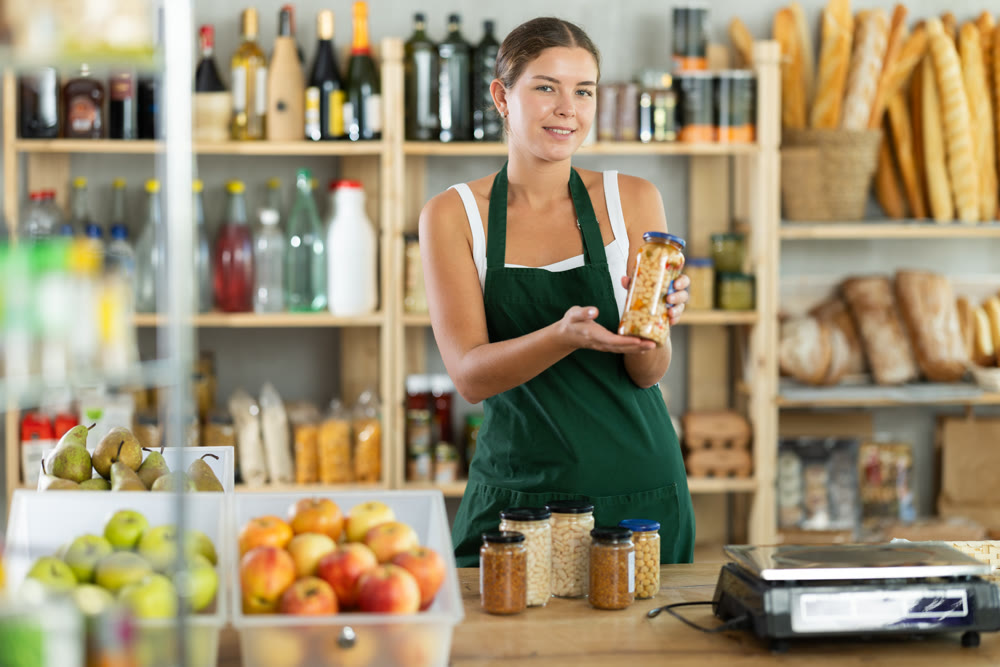 Portrait of friendly girl seller behind a store counter offering to buy canned beans and legumes