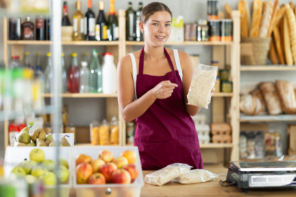 Friendly female salesperson offers to buy oat flakes in produce section of supermarket