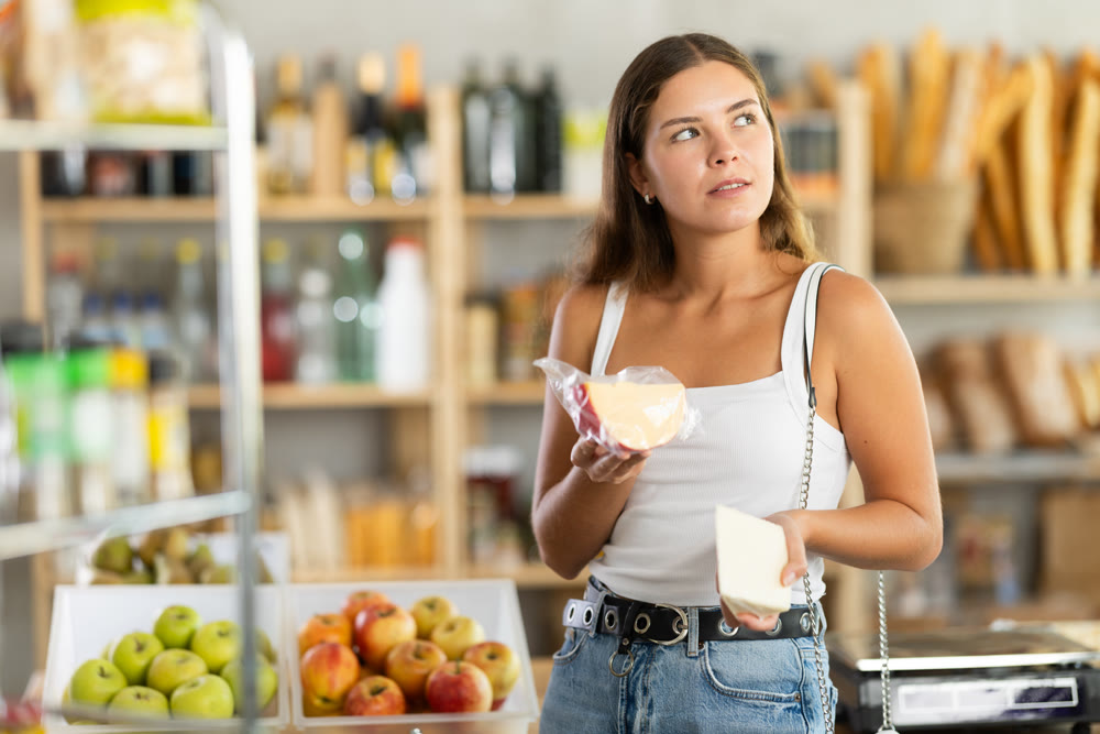 Young woman choosing cheese in grocery store