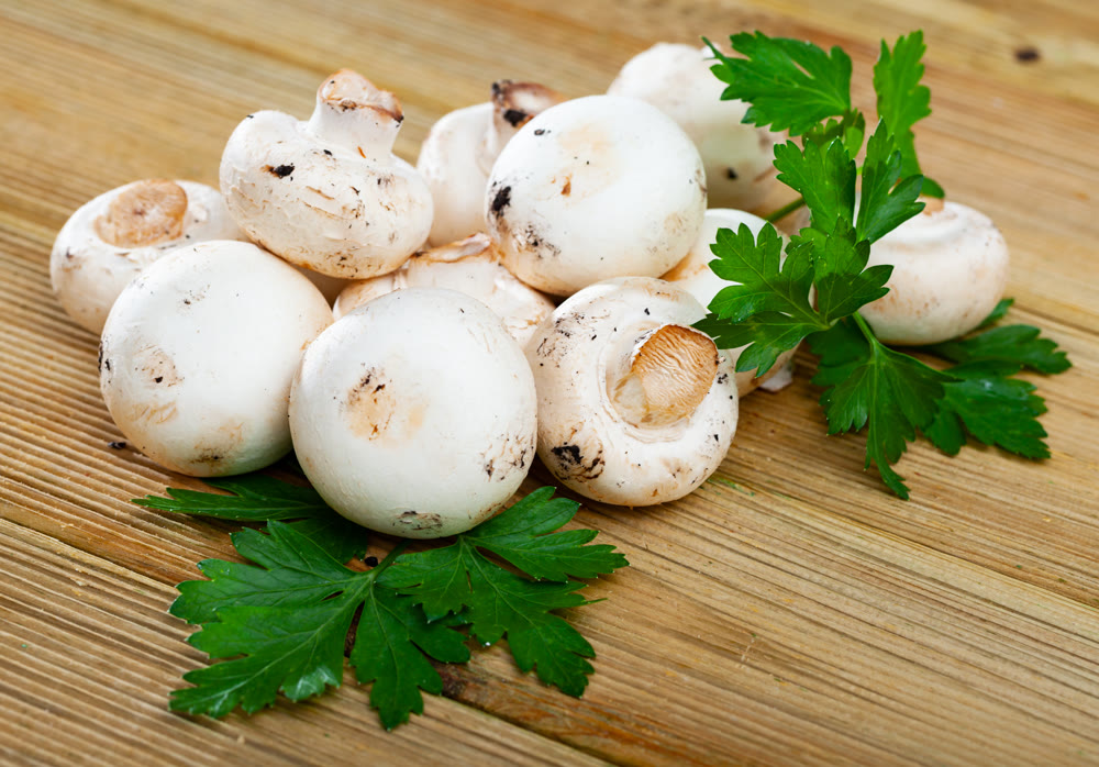Champignons mushrooms on wooden surface with greens
