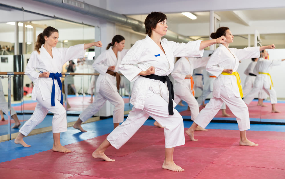 Womens wearing white kimonos standing in attacking stance, practicing movements of close combat punches in training room during martial arts workout