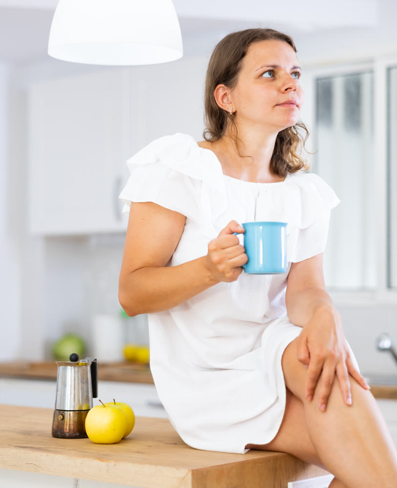 Portrait of young woman in white dress drinking morning coffee in modern kitchen