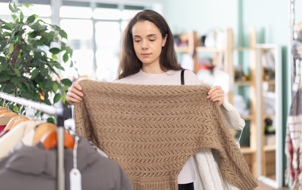 Thoughtful young girl choosing sweater in clothing store