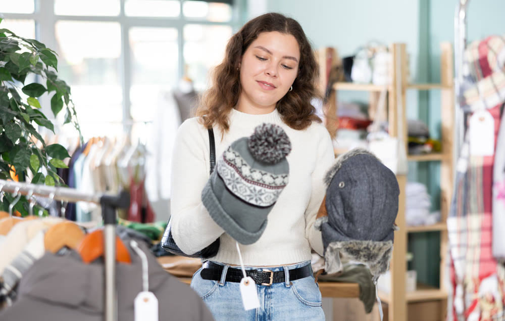 In shop, girl spend time in shop and choose winter hat.