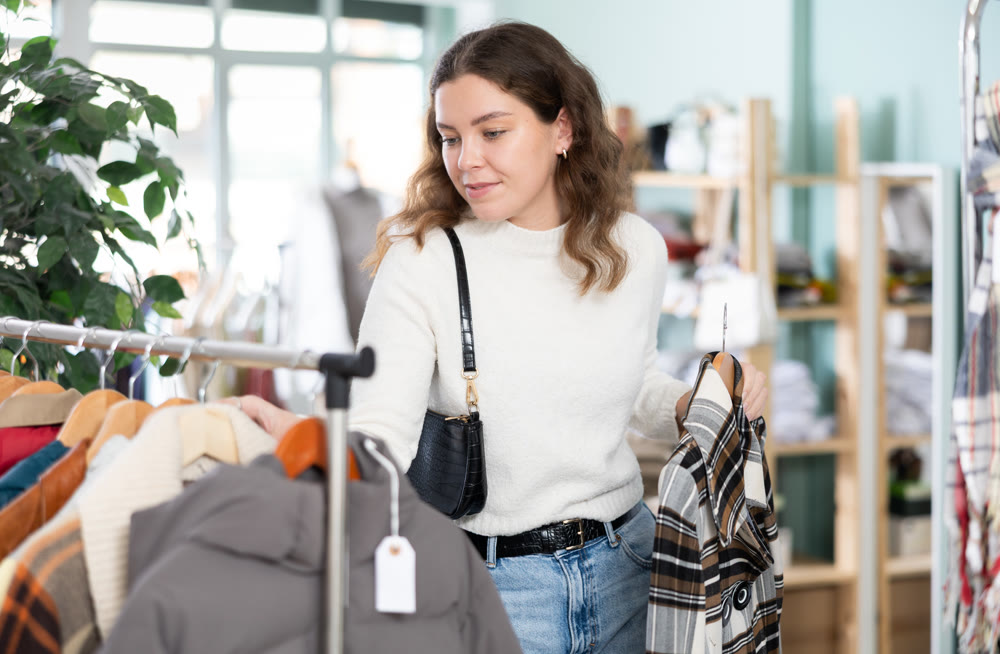 Young woman choosing coat in clothing store