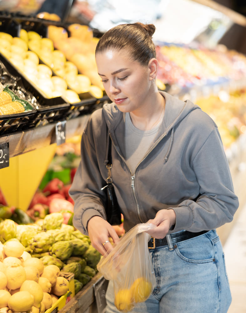 Young woman chooses lemons in vegetable shop