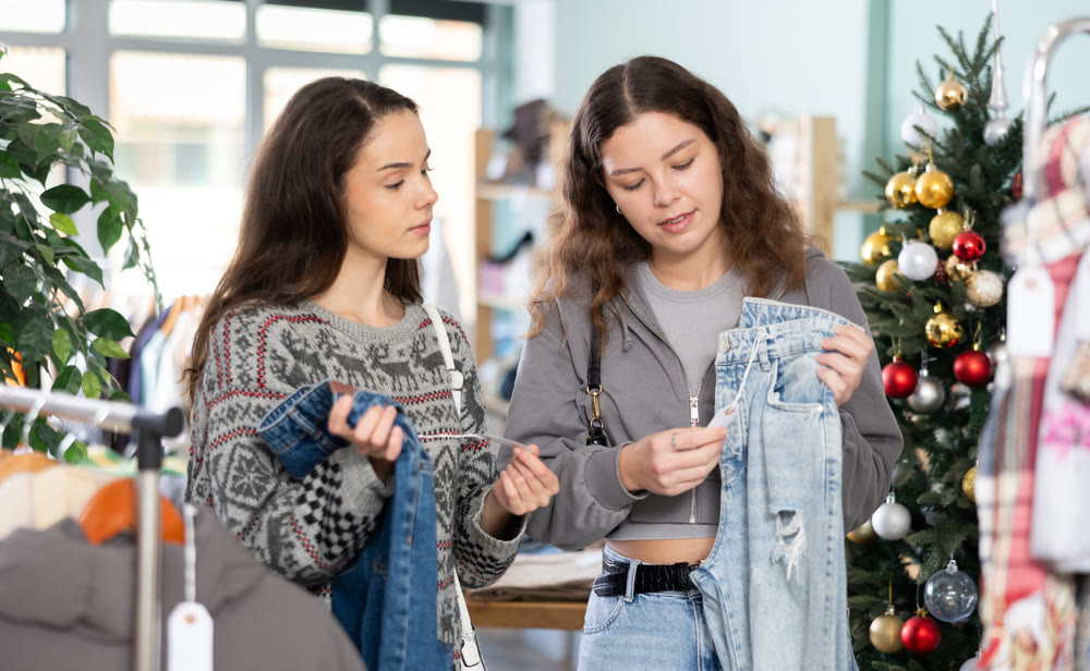 Young girls choosing jeans pantaloons in clothing store during Christmas