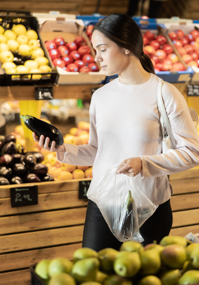 Young woman buyer choosing eggplant at vegetable market