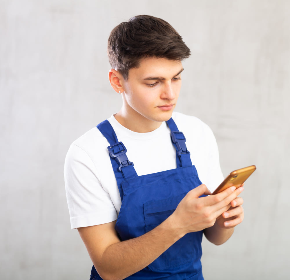 Guy in blue jumpsuit holds smartphone in hands and enthusiastically communicates on social networks