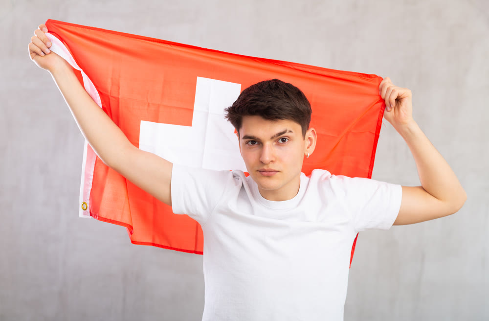 Portrait of calm, balanced young man in casual clothes with fabric of national Swiss flag.