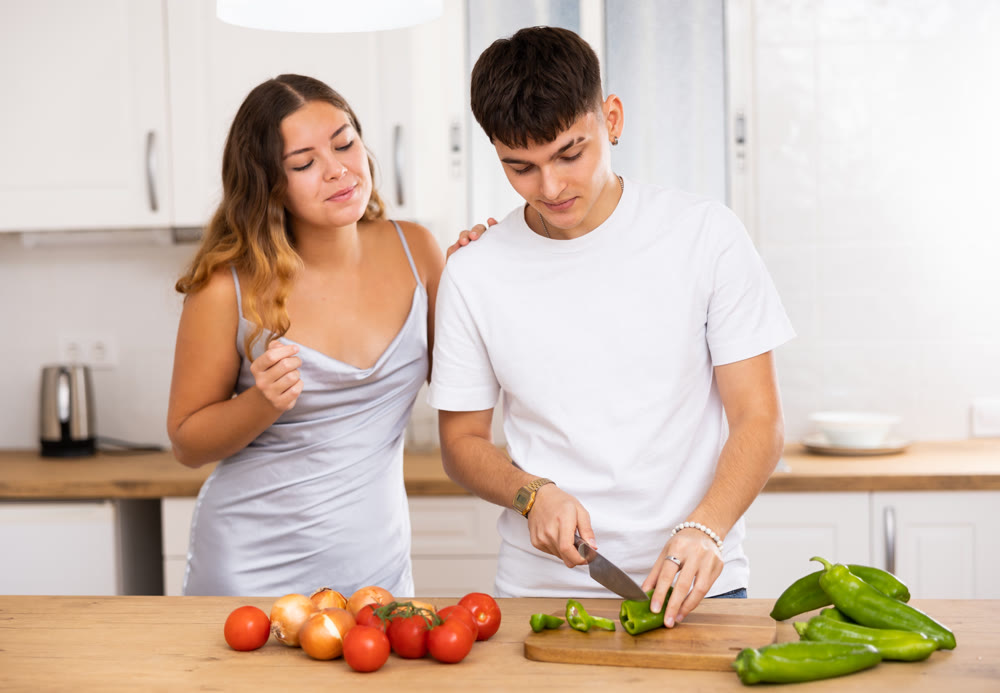 Woman preparing vegetable salad and communicating with her husband in kitchen