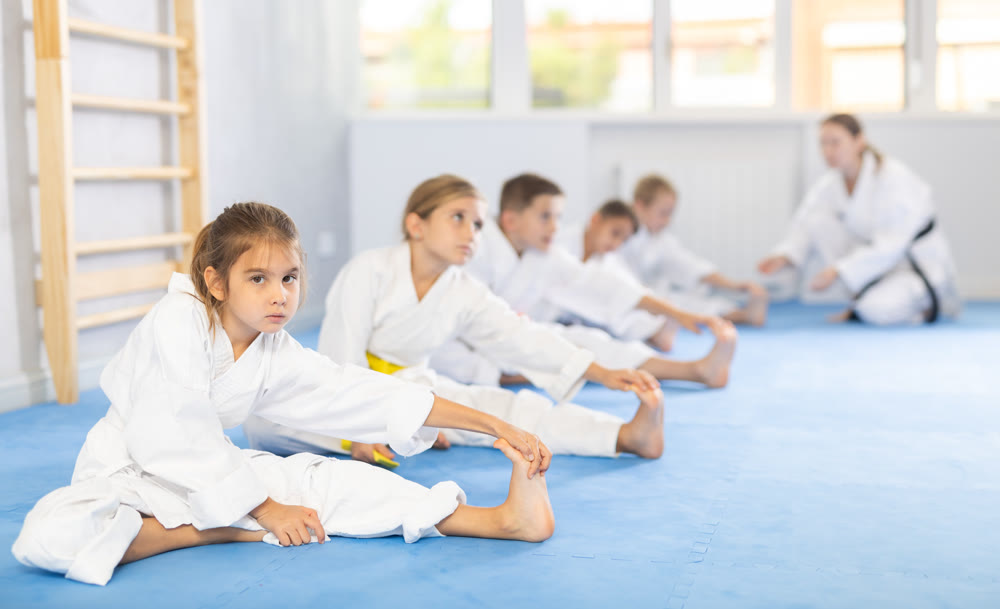 Children in white kimono doing stretching before karate ore judo training