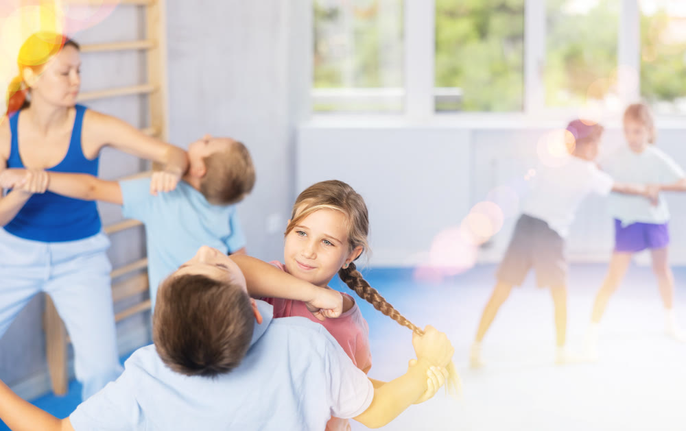 Children practicing in pair self-defence movements with female trainer supervision
