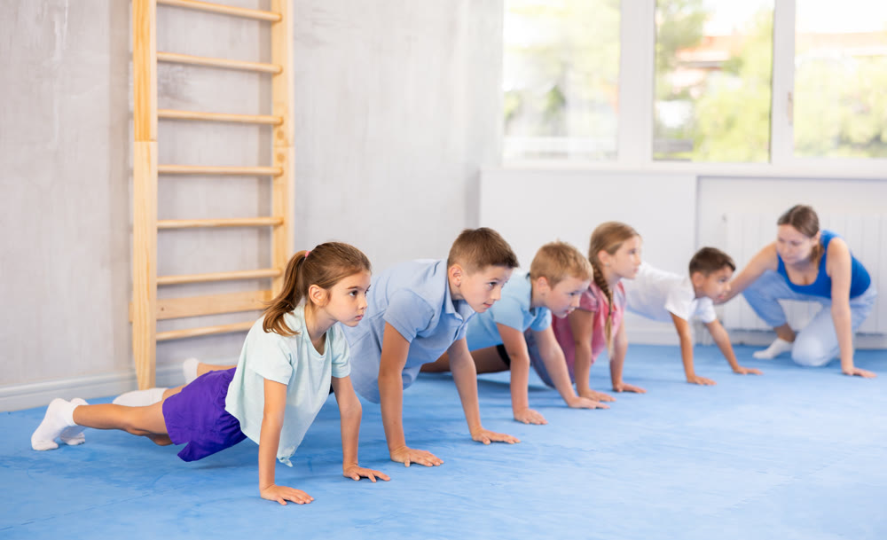 Group of little children doing push-ups on sports mats during a self-defense class in gym
