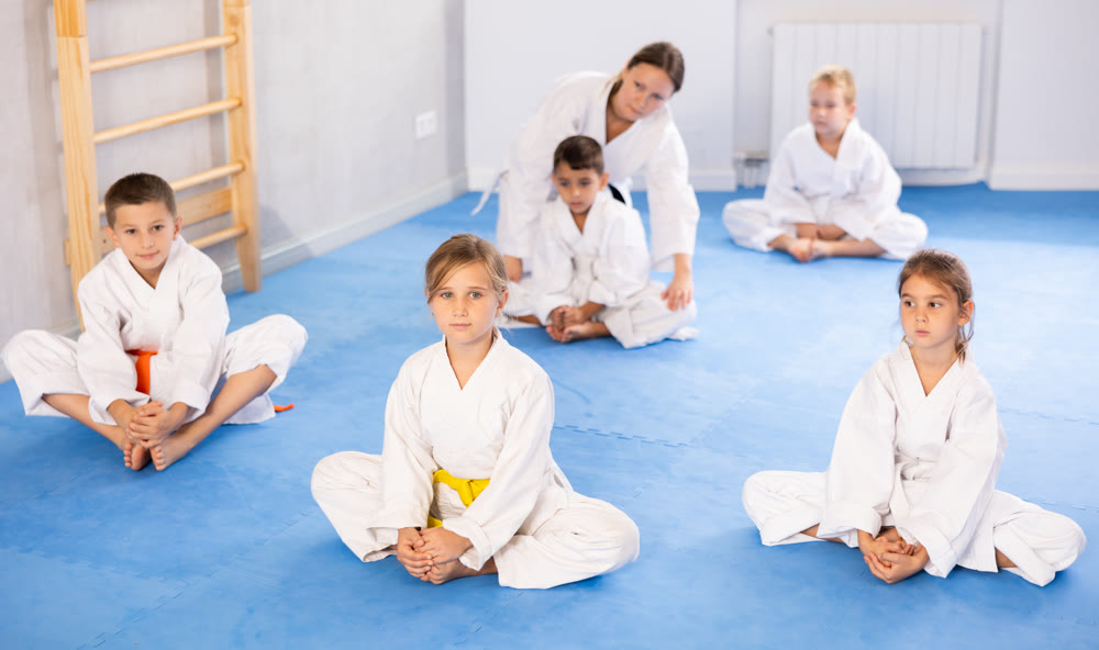 Children before training martial arts performs stretching butterfly with couch help