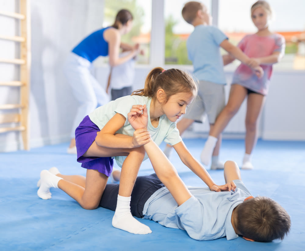 Children practicing in pair self-defence movements with female trainer supervision