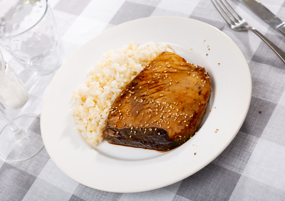 Delicious slightly fried tuna with soy sauce and sesame served on plate with side dish of white rice..