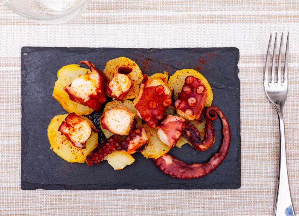 Galician boiled octopus with smoked paprika and potatoes on slate board