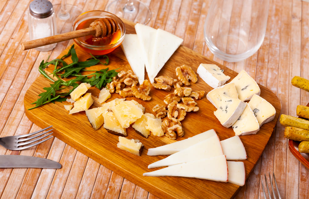 Delicious cheese assorted with honey and walnuts on a wooden board, decorated with fresh arugula