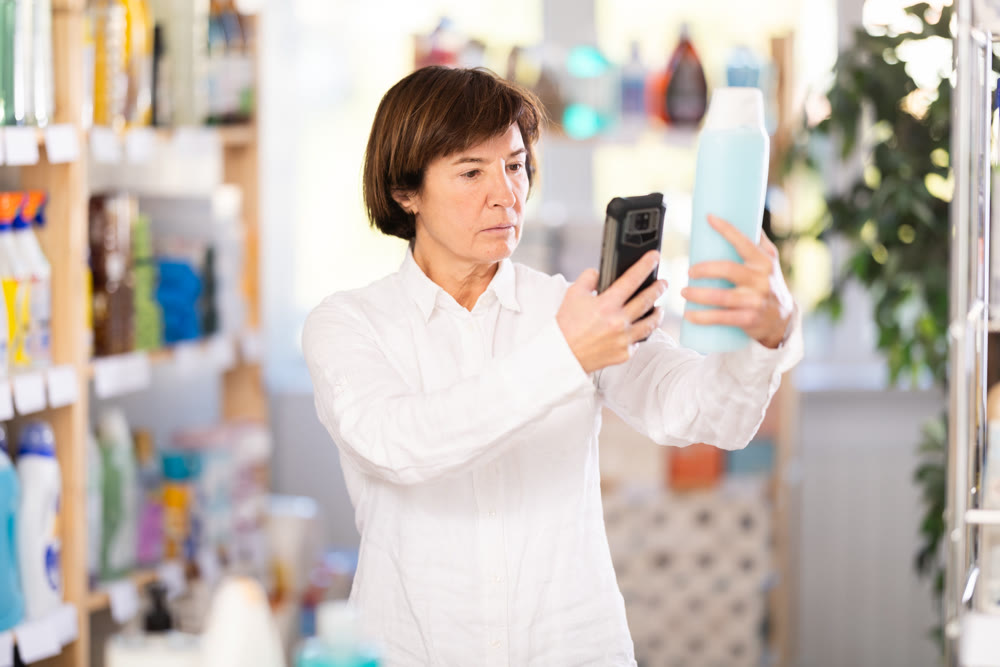 Checking expiration date of shampoo or shower gel - female shopper scans QR code on label of shampoo using smartphone