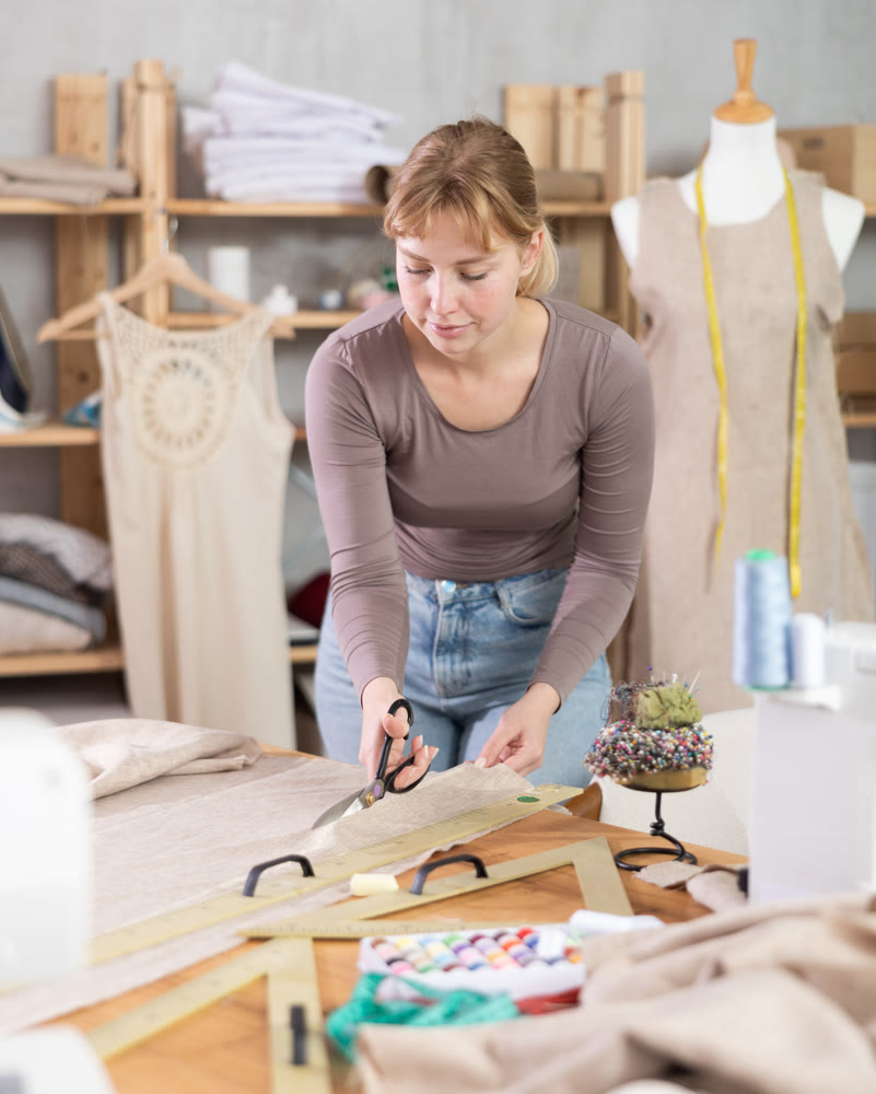 Young female dressmaker cutting textile in sewing workshop