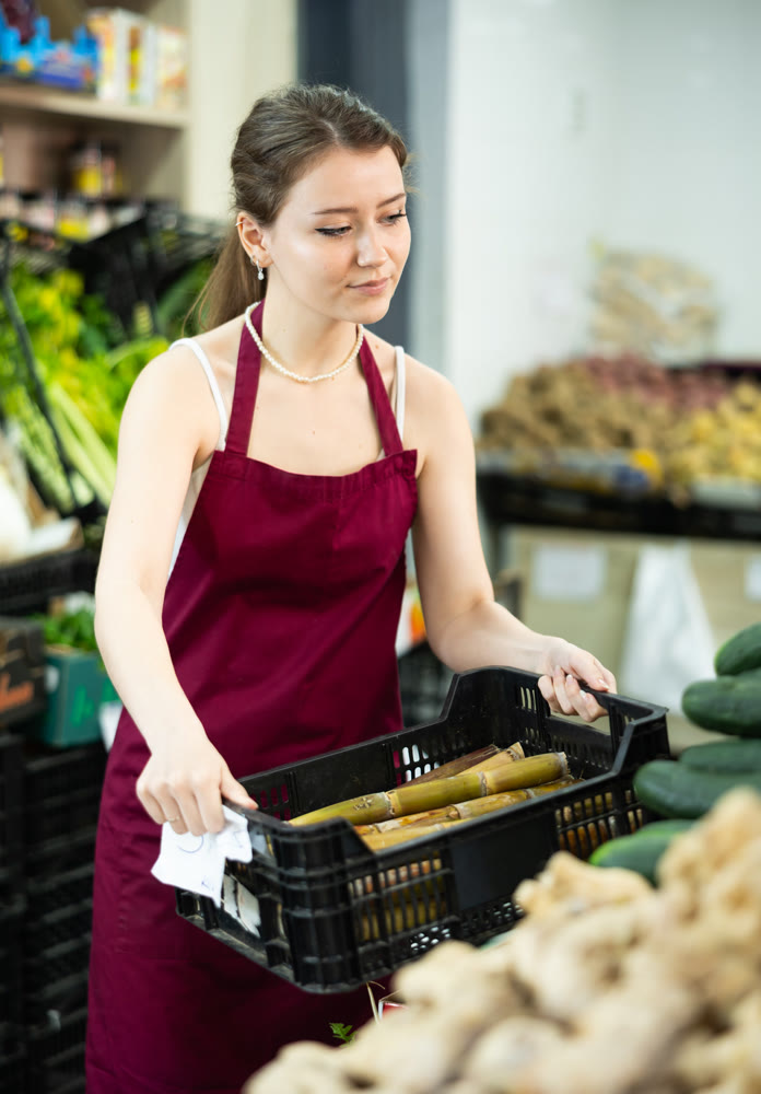 Supermarket employee carefully places asparagus on shelves of supermarket