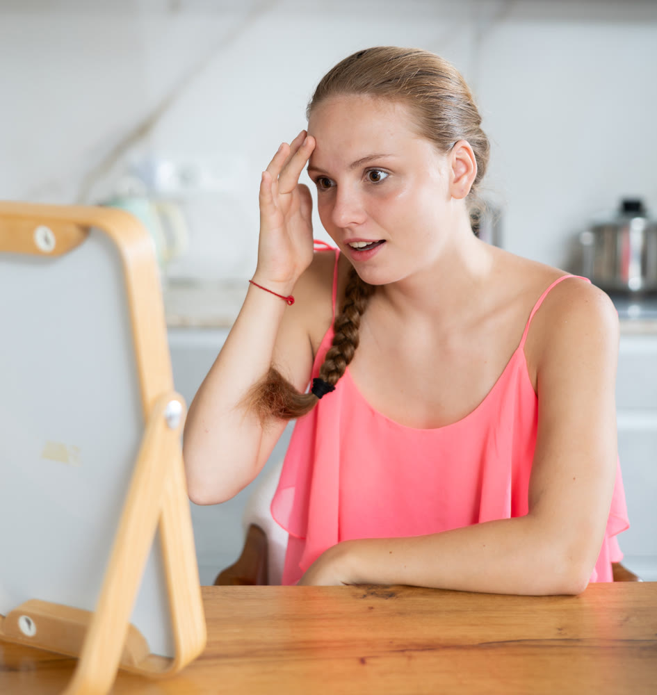 Teenage girl is sitting at kitchen table and looking at her reflection in mirror