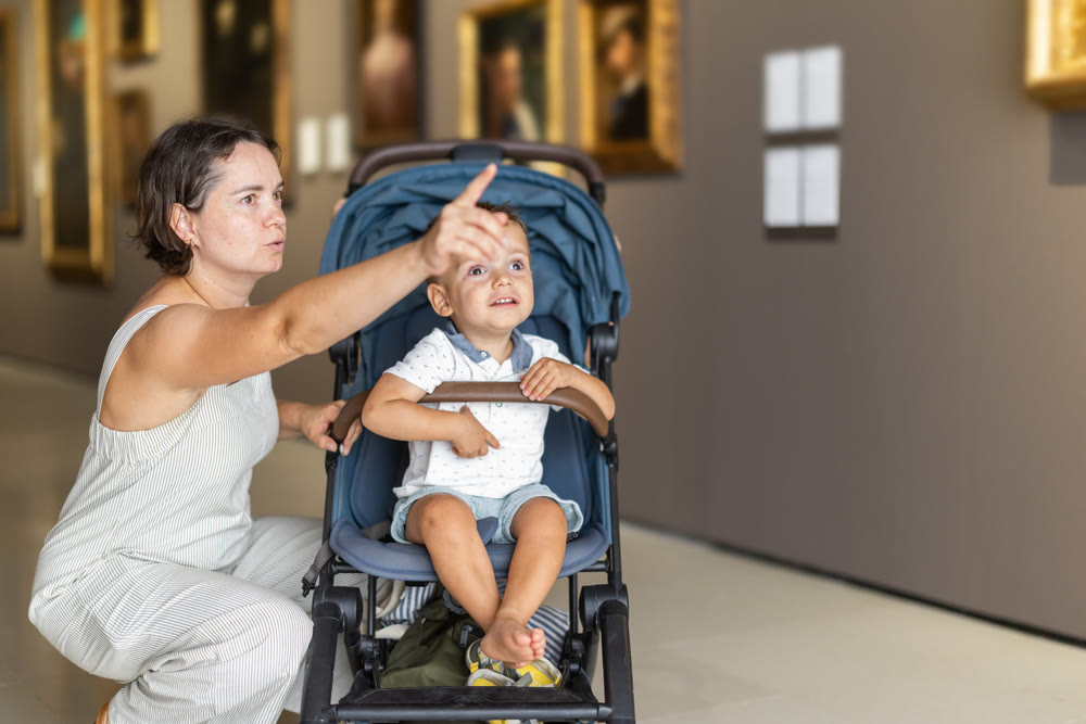 Mother with toddler boy exploring picture exhibition in museum