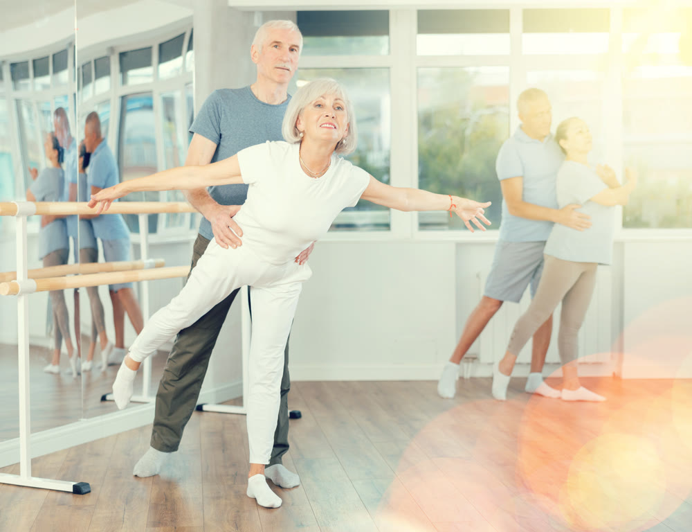 Mature man and woman practicing arabesque position of ballet in pair in dance studio