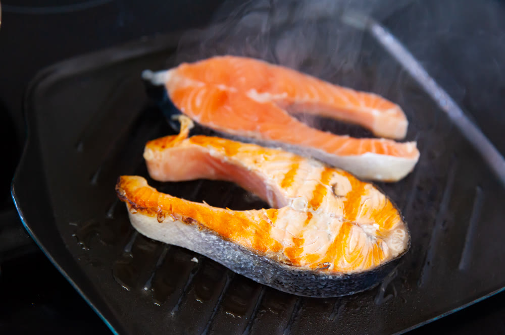 Grilled salmon fillets seasoned with black pepper are cooked on grill
