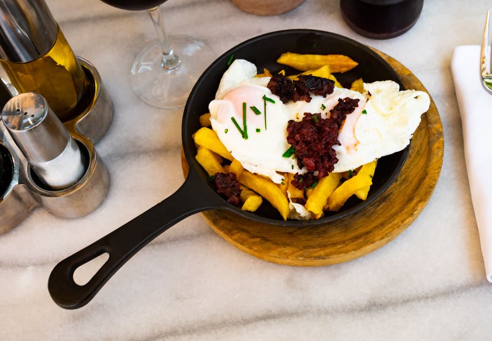 There is portion of French fries, fried eggs and piece of boutifara in pan.