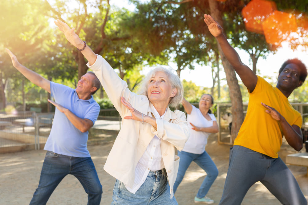 Group of happy women and men different ages practicing dance in summer park