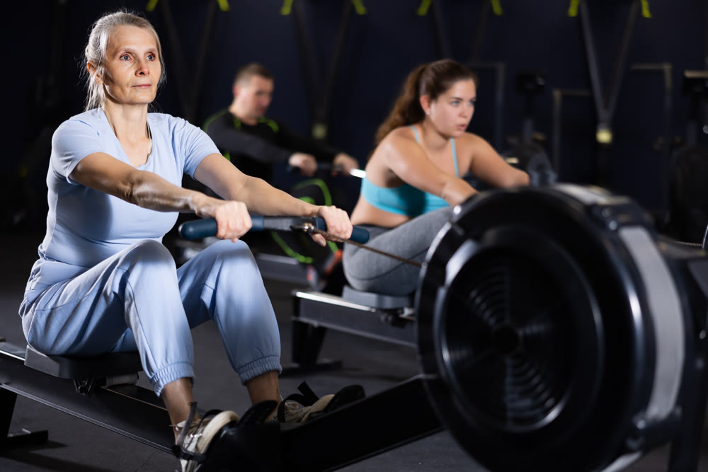 Focused mature female athlete using cable row machine in gym