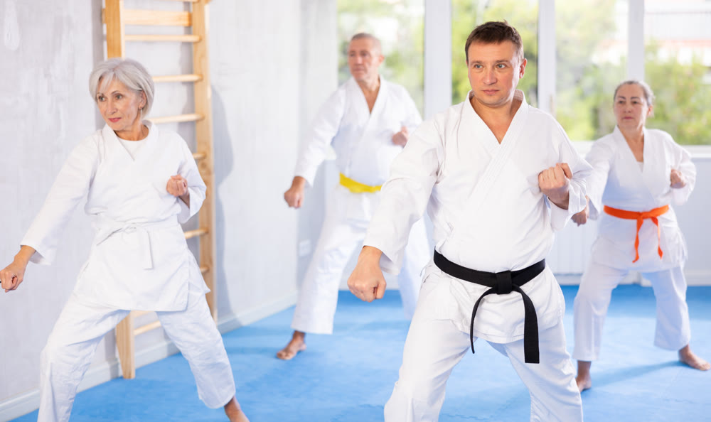 Middle-aged man attendee of karate classes practicing kata standing in row with others