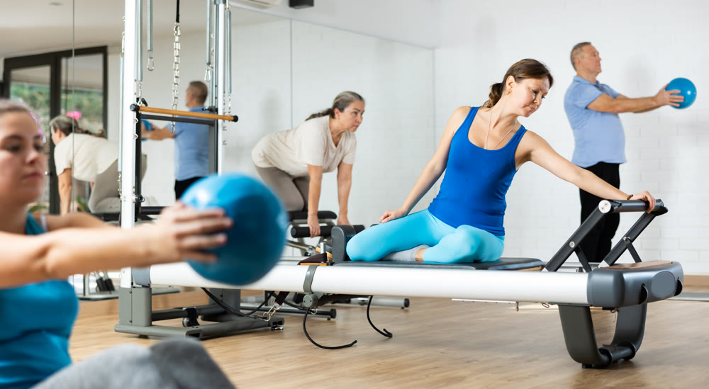 Middle-aged woman practicing pilates on reformer tower equipment in sports hall