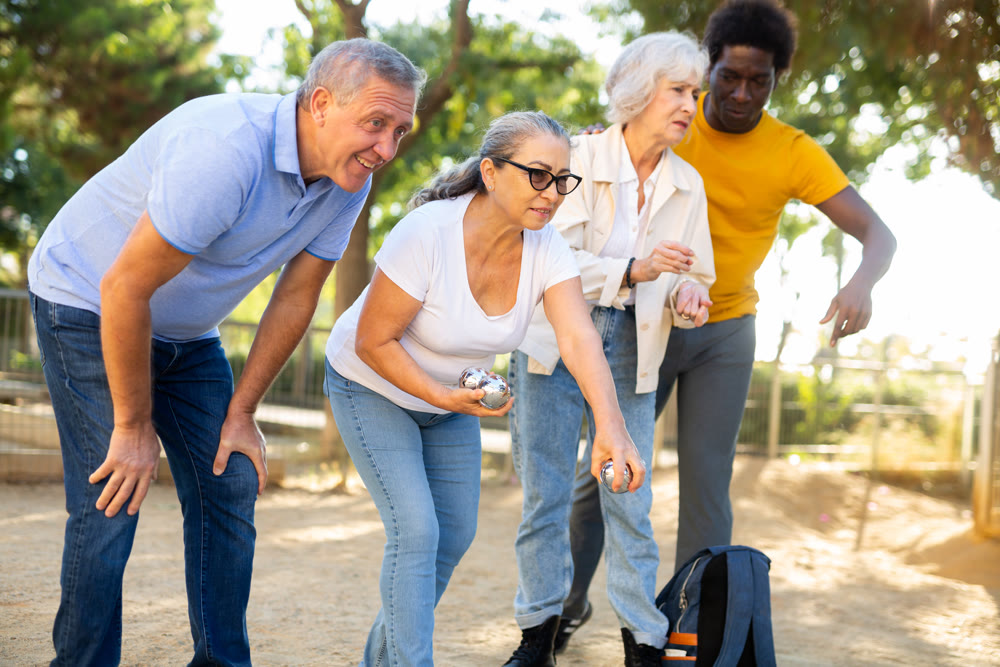 Cheerful males and females playing petanque in park on holidays