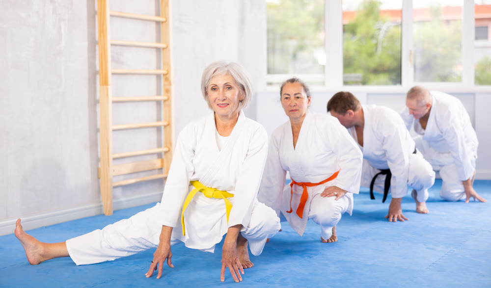 Old woman wearing kimono practicing leg stretching position in sports hall