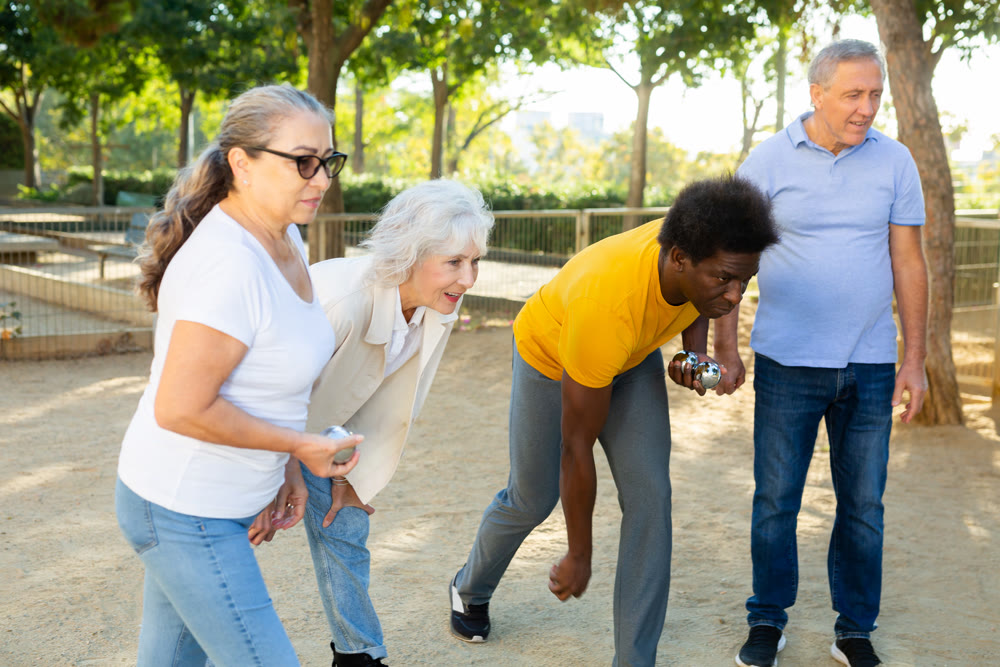 A group of multiracial mature adult people playing patanque game outdoors in a park