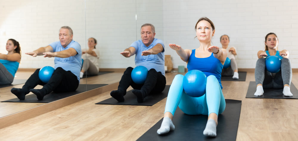 People of different ages pressing core and clutching mini Pilates balls between legs during Pilates training together