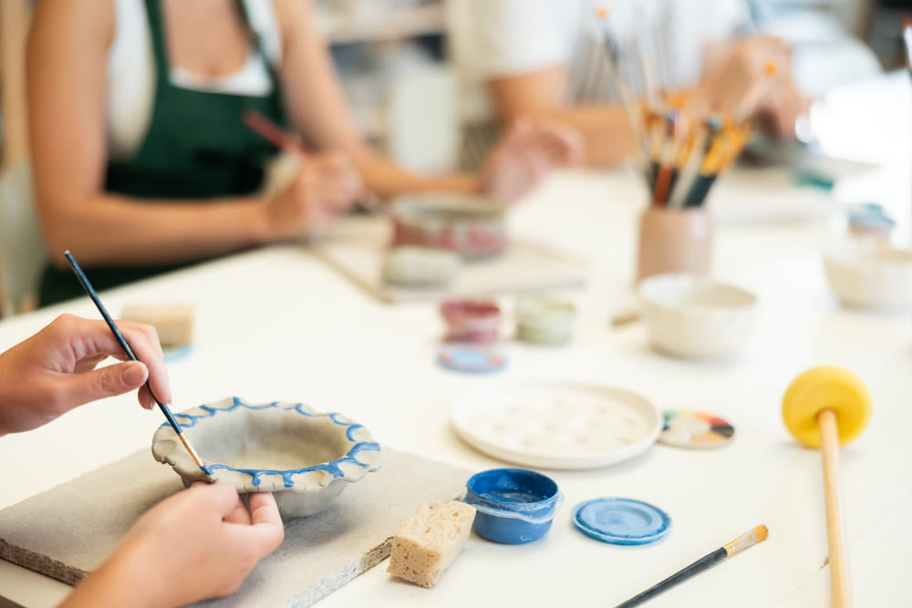 Girl hands paints bowl of clay during master class, close up