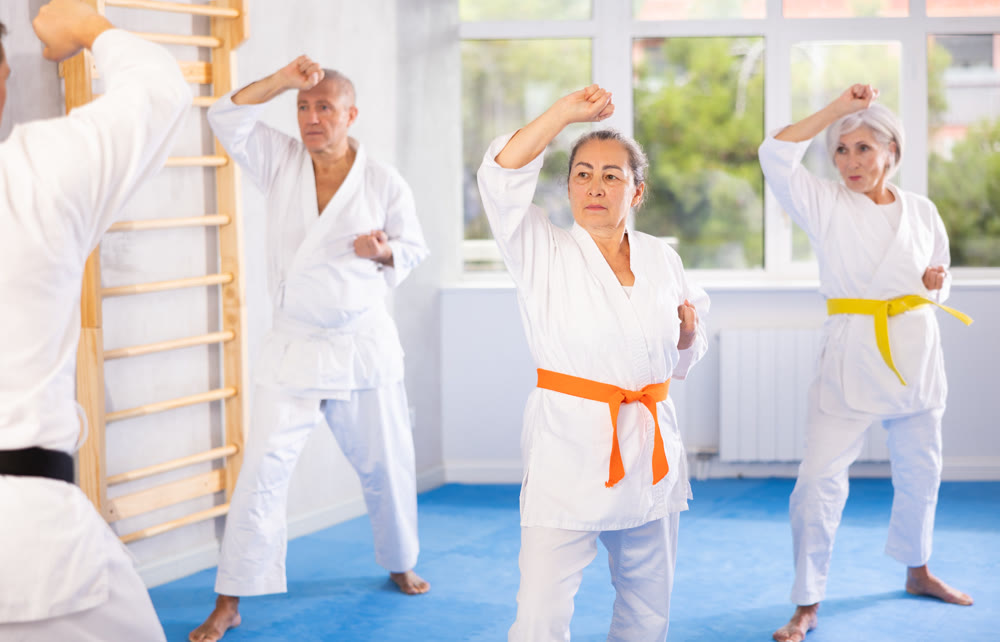 Group of elderly people in white kimonos learn to punch and kick under the guidance of trainer. Karate lessons