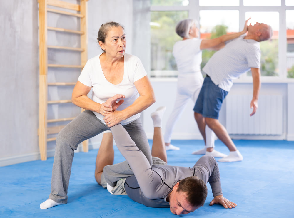 Senior woman in pair with middle-aged coach train Krav Maga and self-defense skills.