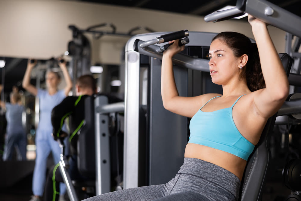 Sporty young woman using overhead press machine in gym